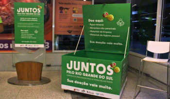 Baú onde as doações são arrecadadas. No corpo, há o texto "Juntos pelo Rio Grande do Sul" e lista das prioridades de doação para a campanha: água mineral, alimentos não perecíveis, itens de higiene pessoal e material de limpeza.